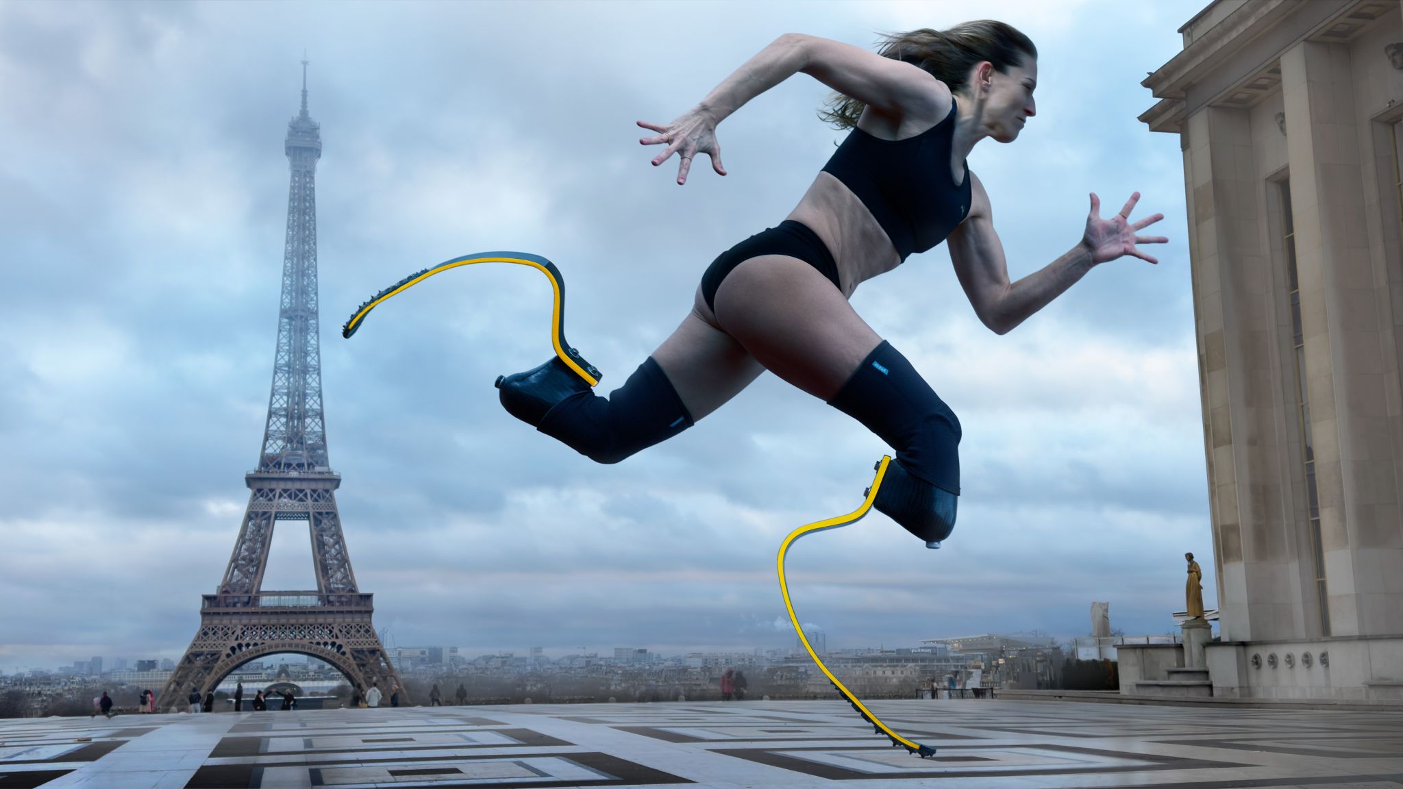 Para Athlete Sara Andrés Barrio with running blades is mid-stride in front of the Eiffel Tower. She wears a sports bra and shorts. The background features a cloudy sky and Parisian architecture.